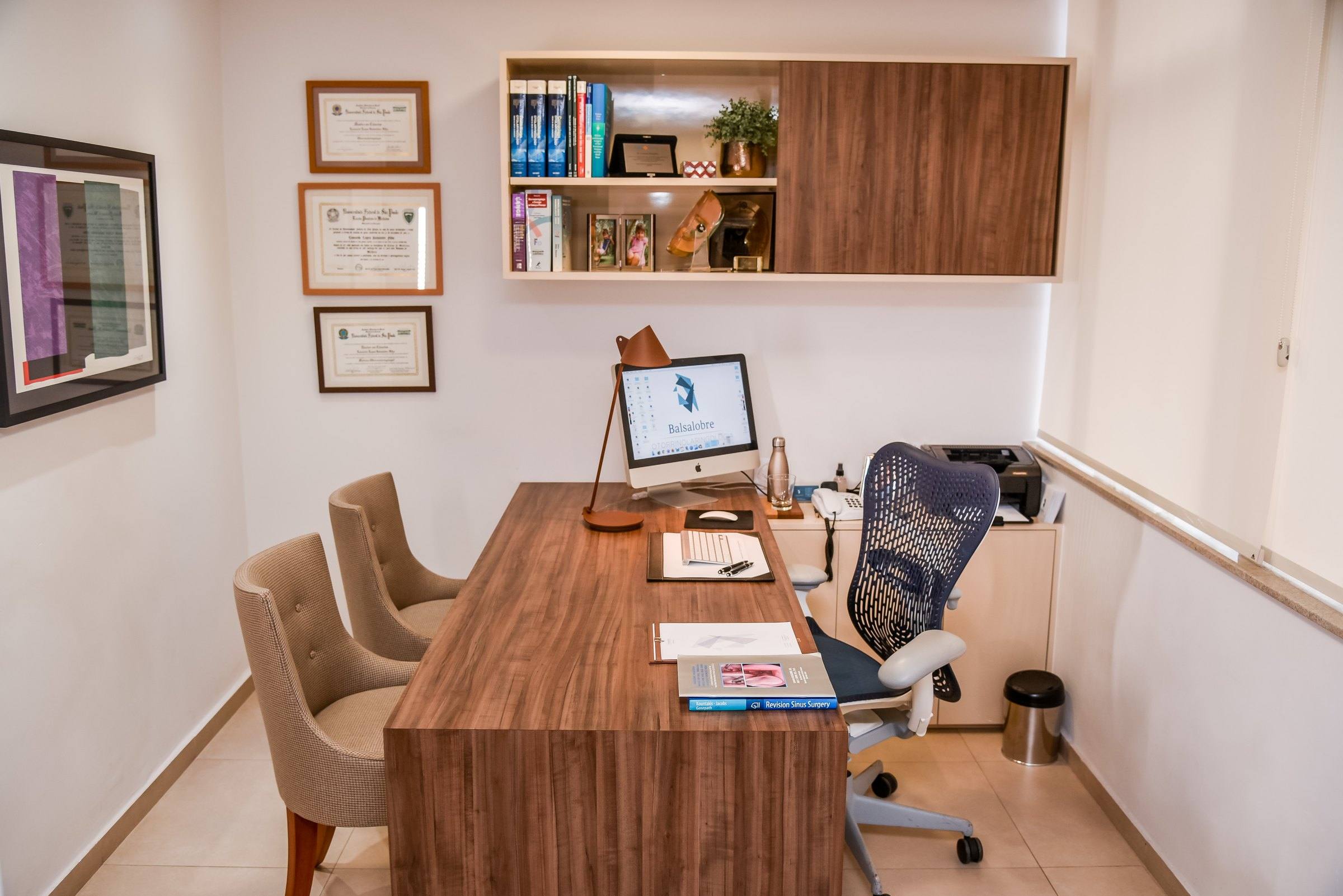 Consultório do Dr. Leonardo, com mesa de madeira, luminária e diplomas na parede