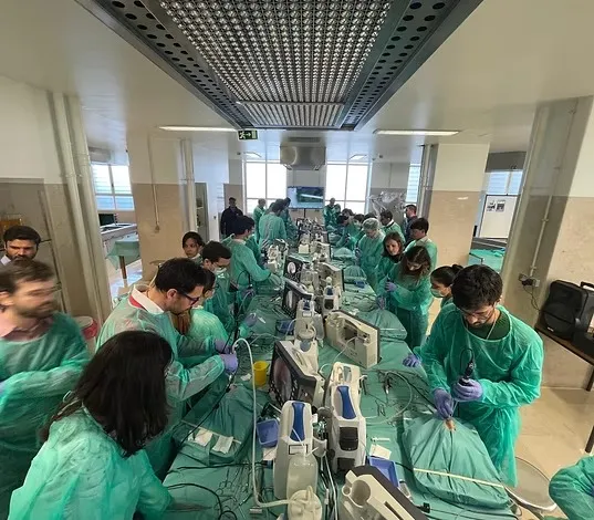 Alunos de avental verde treinando em bancadas com monitores de vídeo