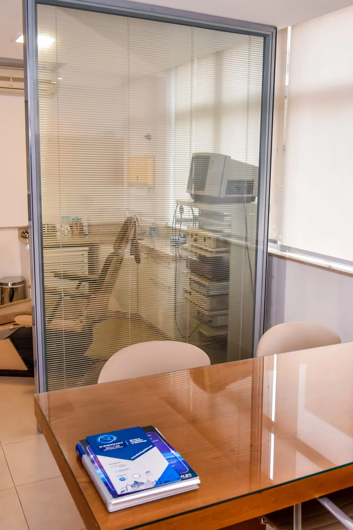 Consultório com divisória de vidro e sala de exame ao fundo